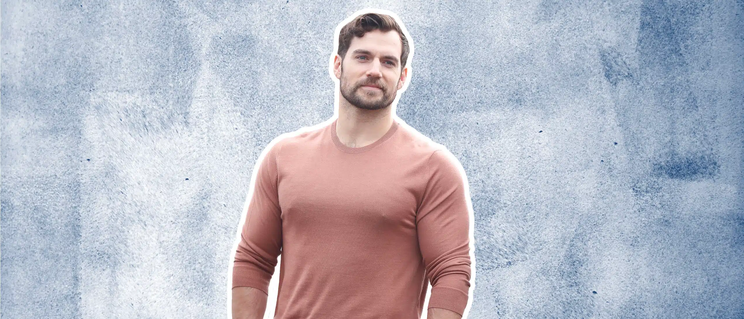 Henry Cavill with a sly smile on a grey background