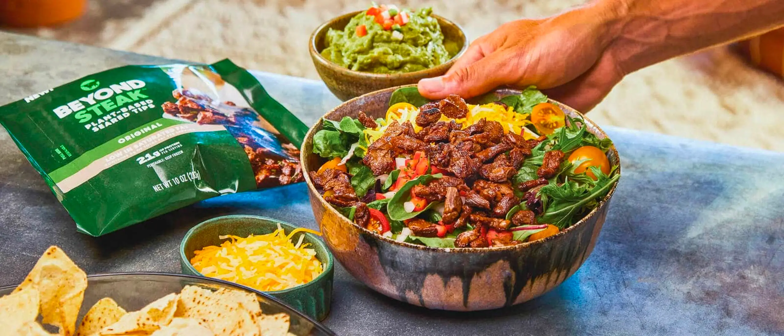 man holding steak salad bowl with chips and guacamole
