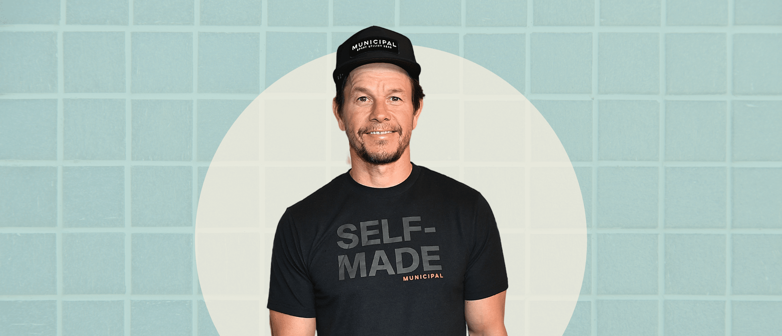 Mark Wahlberg smiling with a blue background and a spotlight around him.