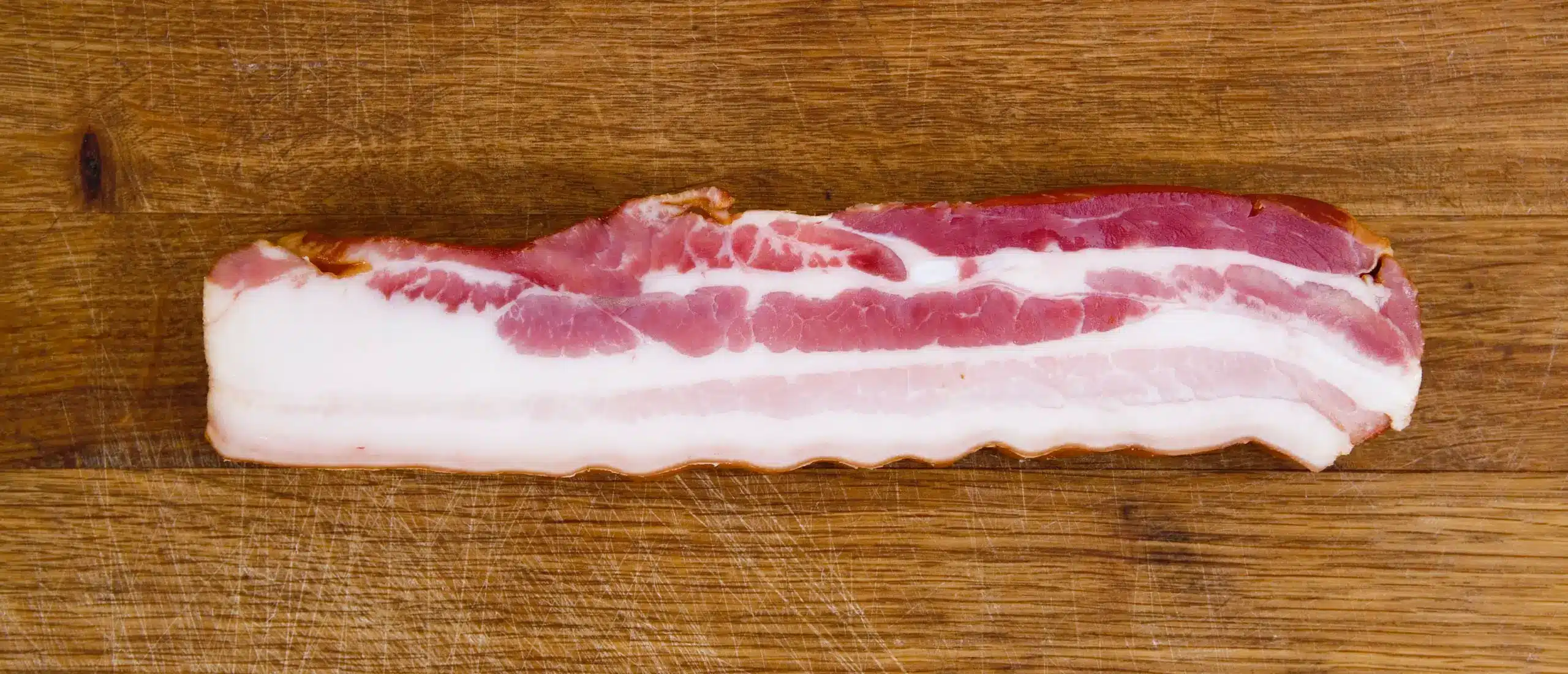 slice of thick fatty bacon on a wooden cutting board