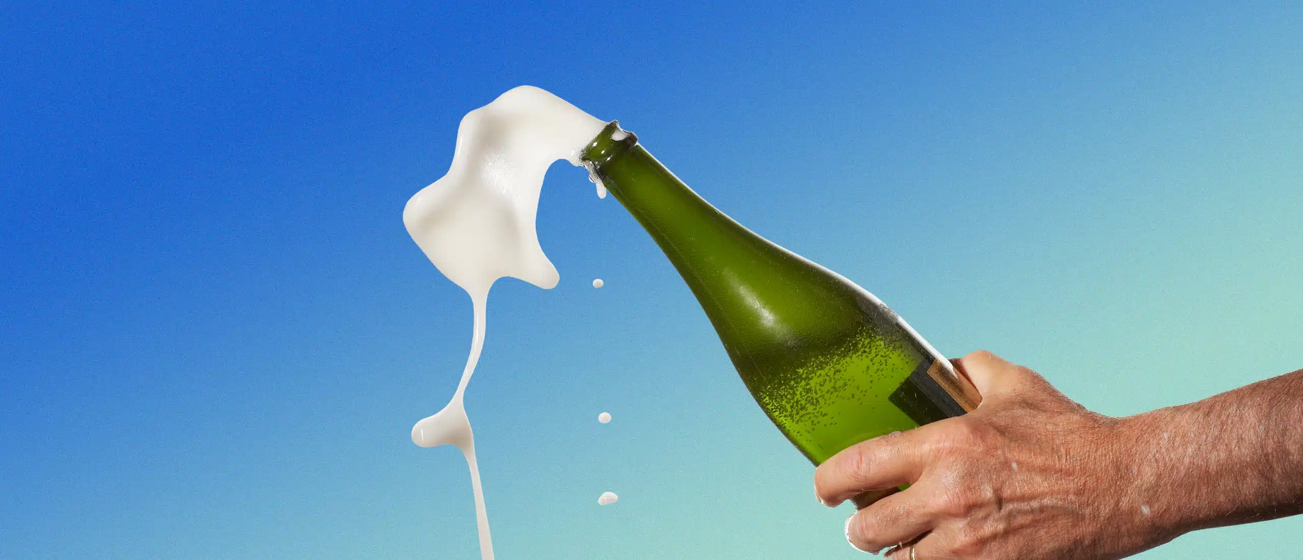 Hands popping a champagne bottle with foam exploding out of the top.