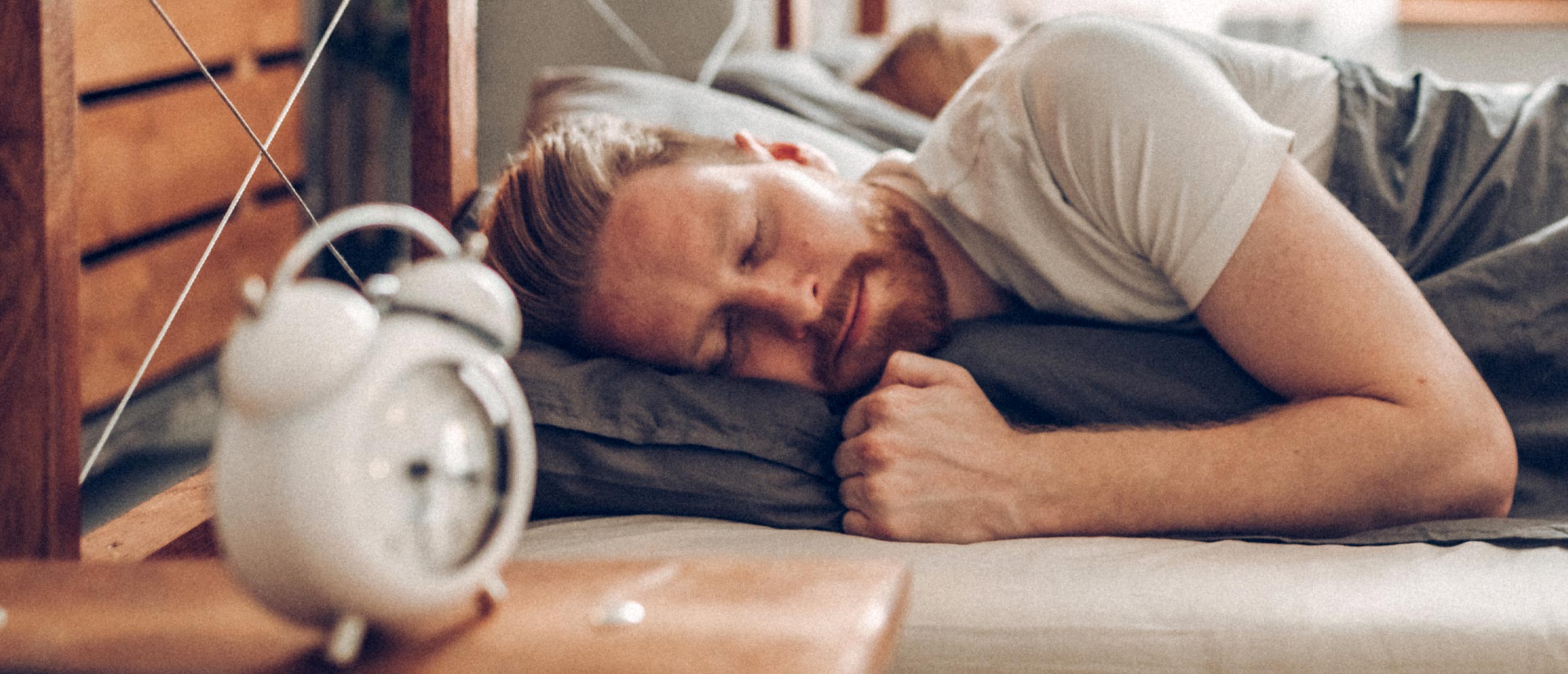 man sleeping on his side next to alarm clock