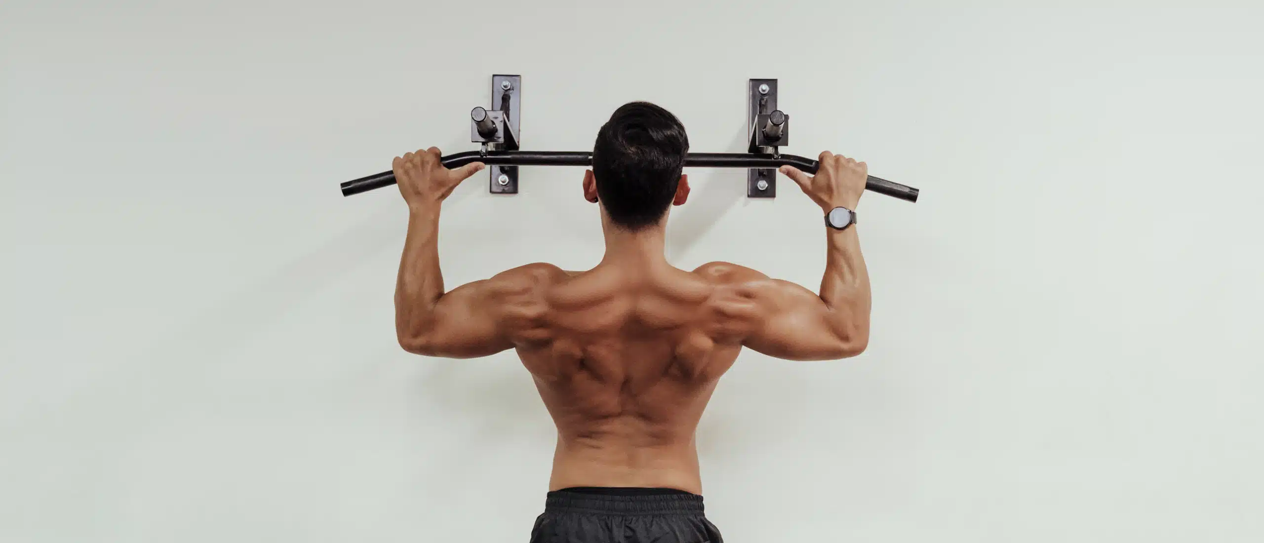 man does pull up on a mounted pull up bar. his back muscles are defined