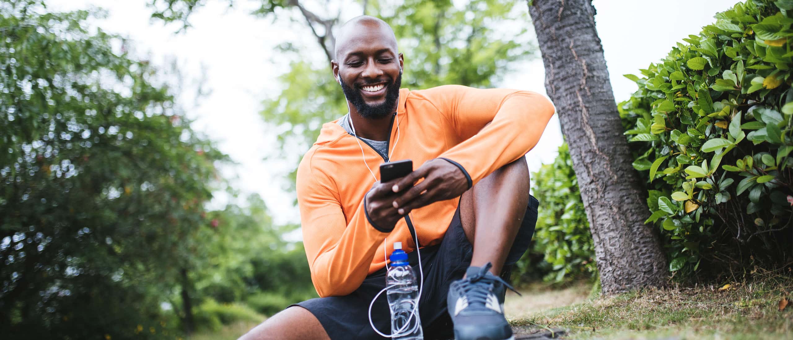 Man sitting down after workout looking on phone smiling