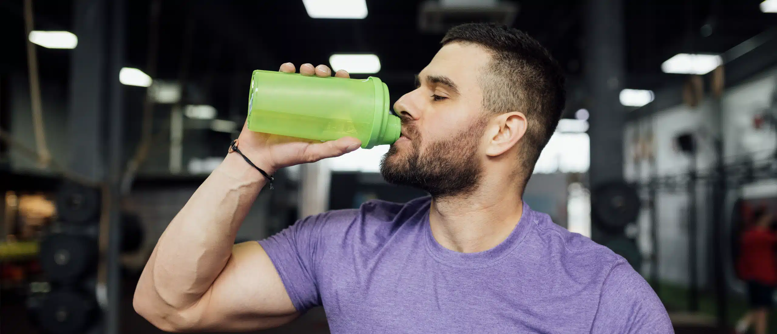 Man drinking creatine from water bottle in gym