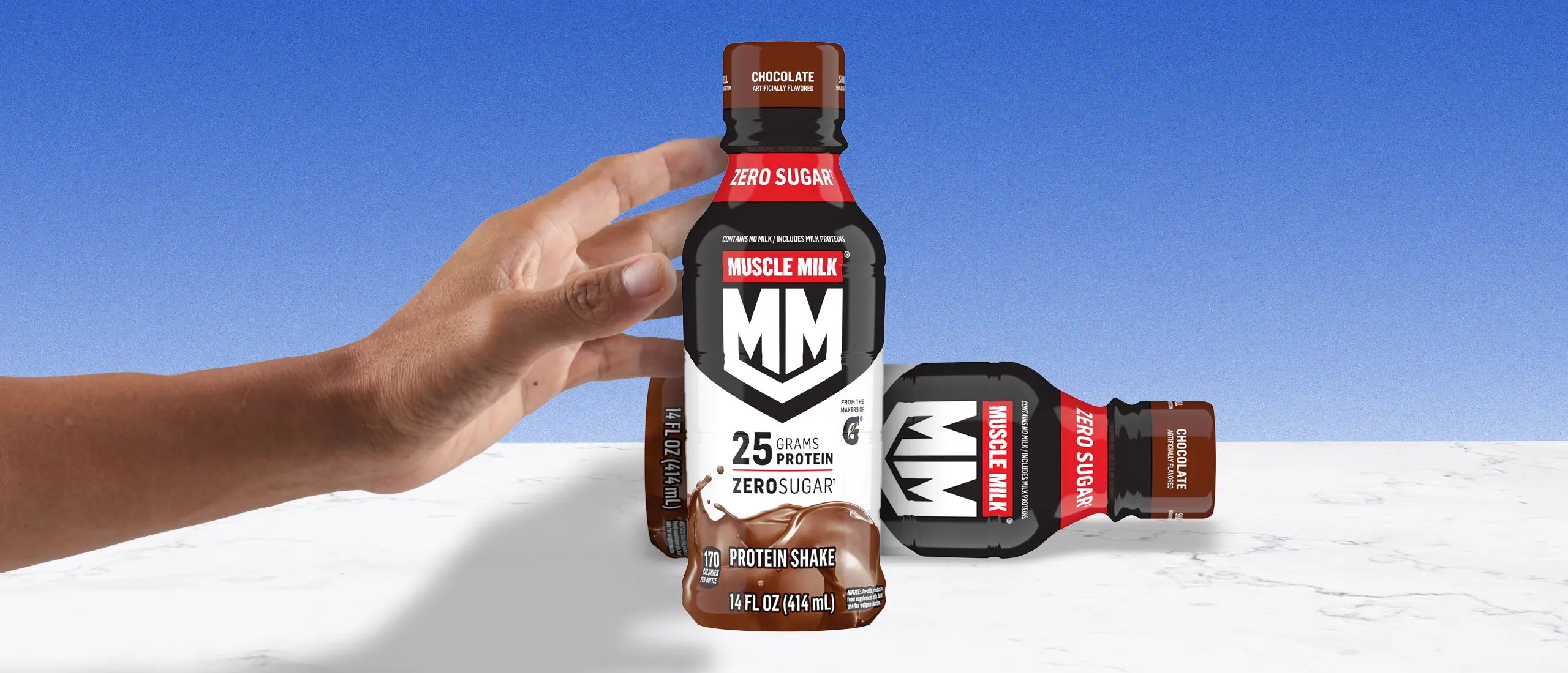 A hand reaching for a bottle of Muscle Milk